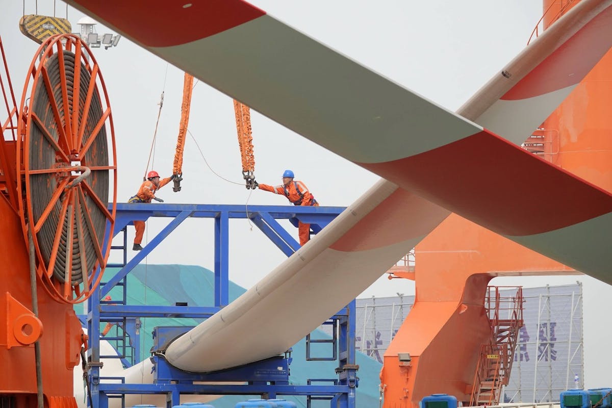 China Windenergie, Wirtschaft, Erneuerbare Energien, Klimawandel, Energiewende: Verschiffung von Offshore-Windkraftanlagen Arbeiter befestigen ein Hubseil an einer Offshore-Windturbinenhalterung im Hafengebiet Penglai des Hafens Yantai 