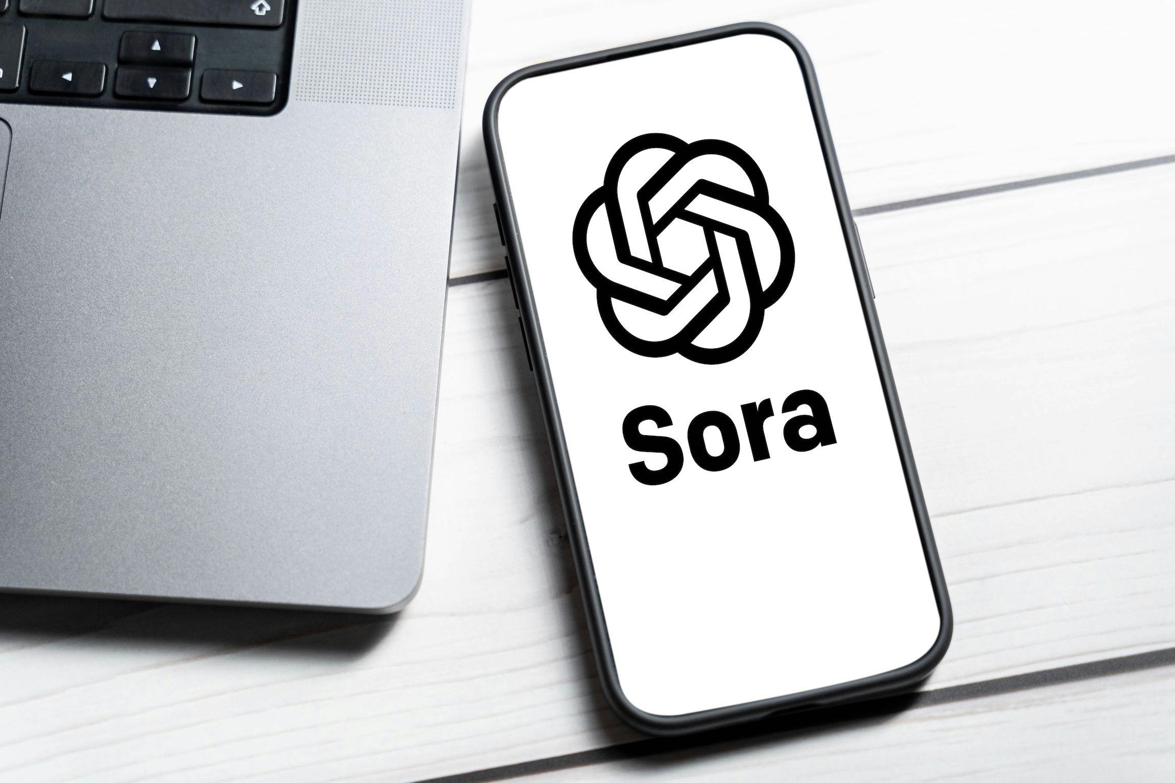 China Technology: Ein Smartphone liegt neben einem MacBook und zeigt das Logo von Sora. Artificial Intelligence, Künstliche Intelligenz, in China
