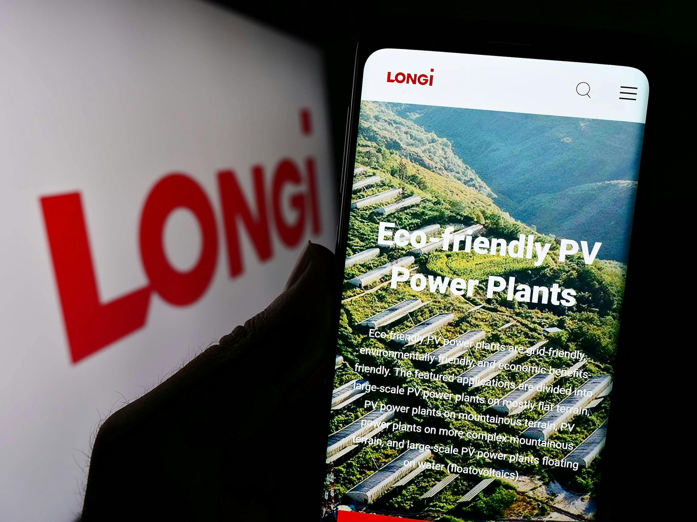 Eine Person hält ein Mobiltelefon mit der Website des Unternehmens LONGi Green Energy Technology Co. Ltd. auf dem Bildschirm.
