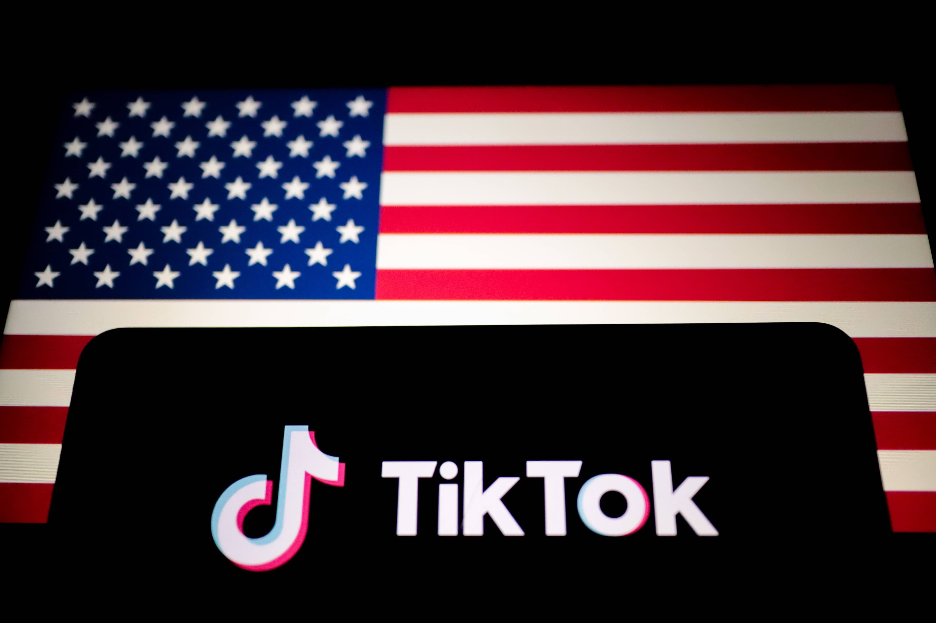 Das TikTok-Logo wird auf einem Smartphone neben der Flagge der USA angezeigt.