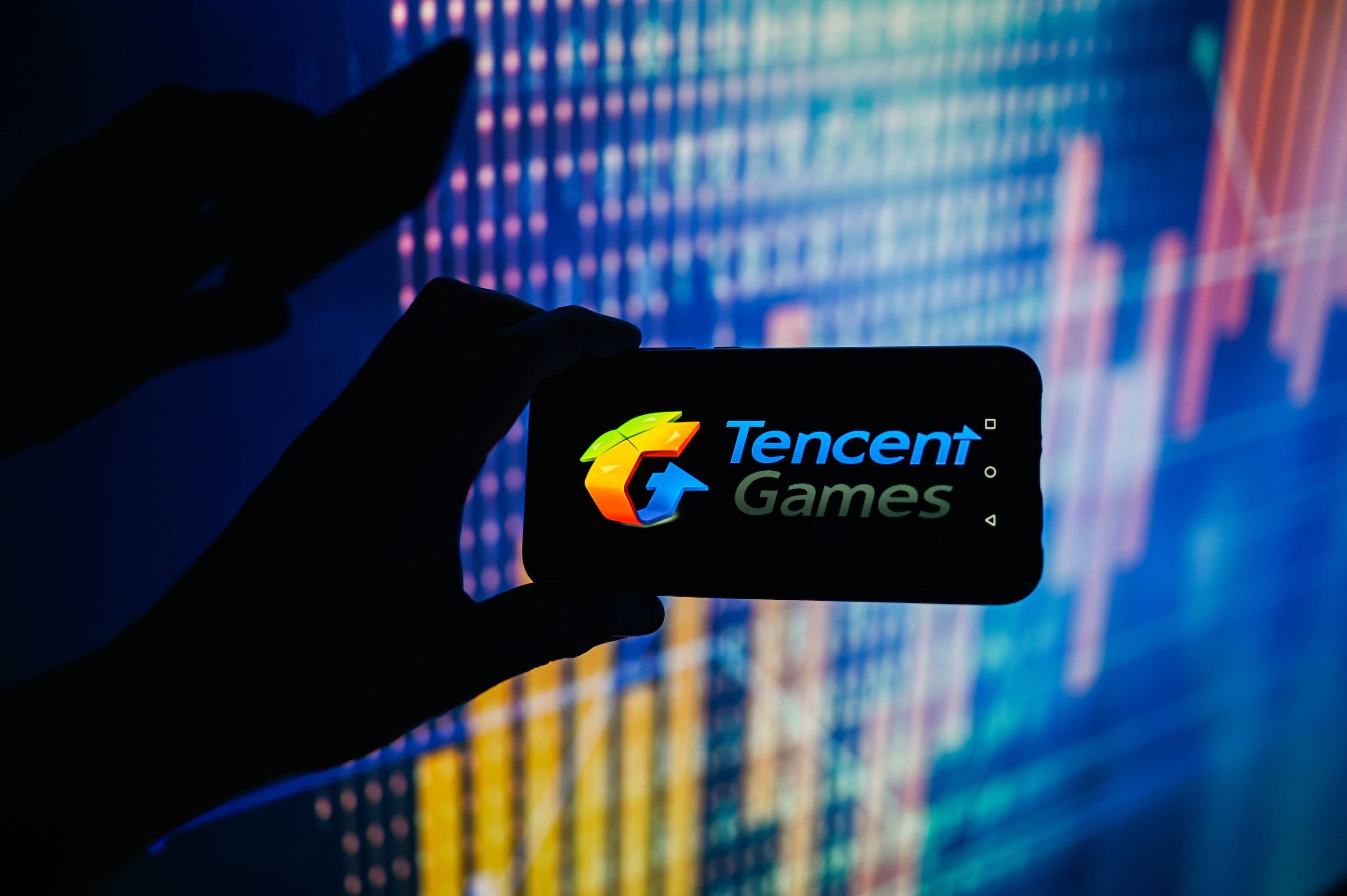 China Aktien, China Wirtschaft, China Stocks:  In dieser Fotoillustration wird ein Tencent Games-Logo auf einem Smartphone mit Börsenkursen im Hintergrund angezeigt