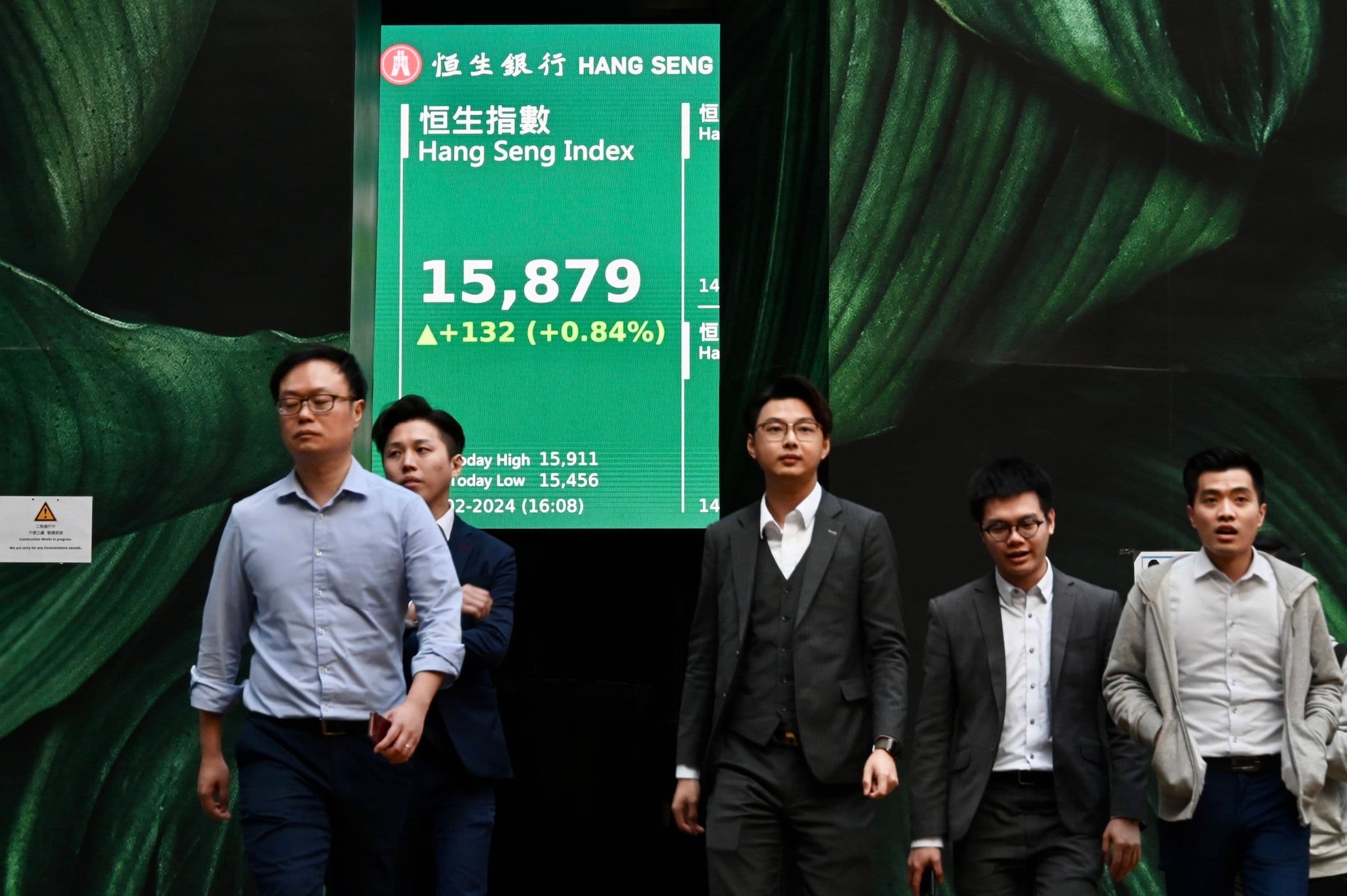 China Aktienmarkt, Aktien, Wirtschaft: Fußgänger gehen vor einem großen elektronischen Bildschirm, auf dem die Zahlen des Hang Seng Index angezeigt werden
