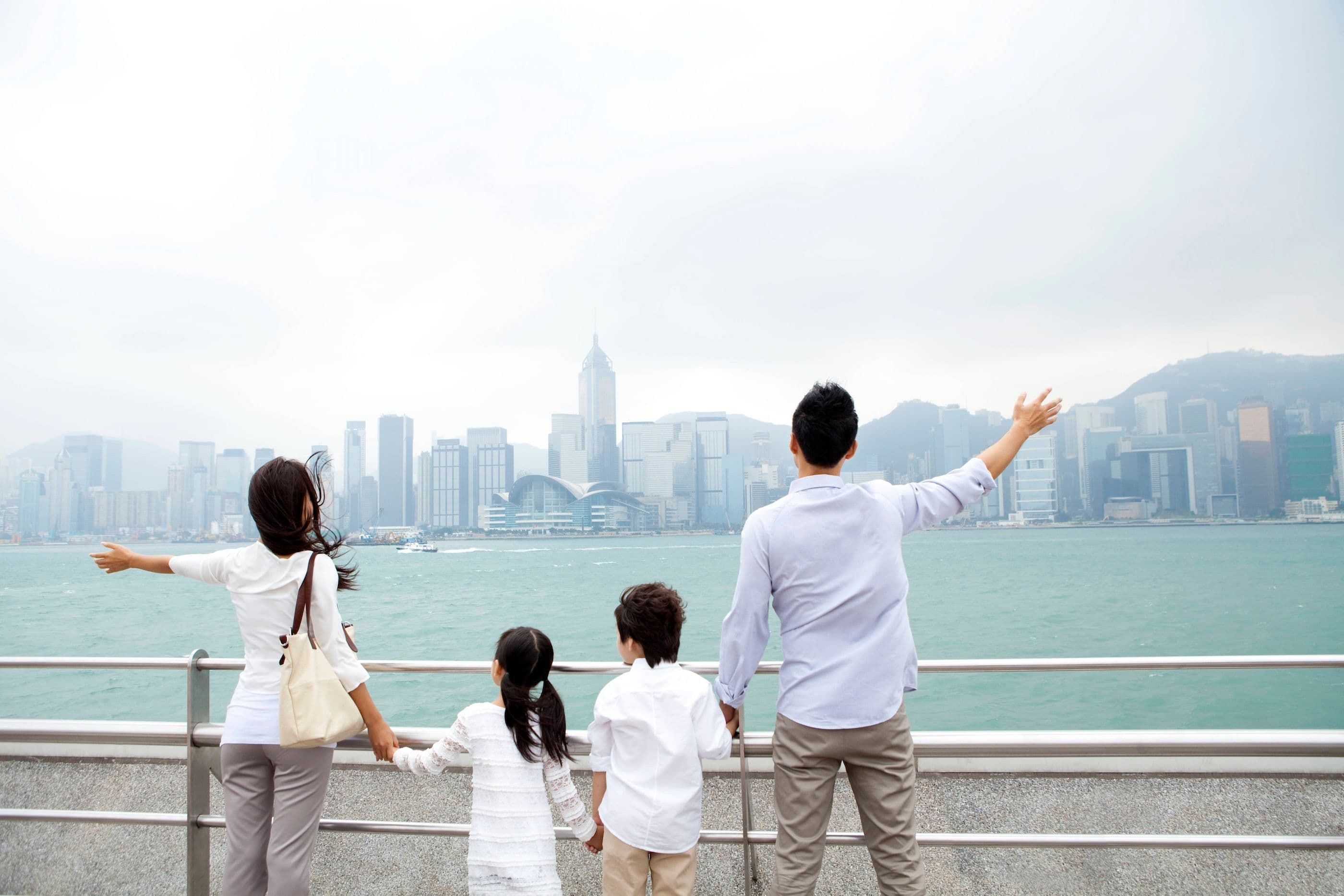 Eine junge chinesische Familie steht am Victoria Harbour und schaut auf die Skyline von Peking