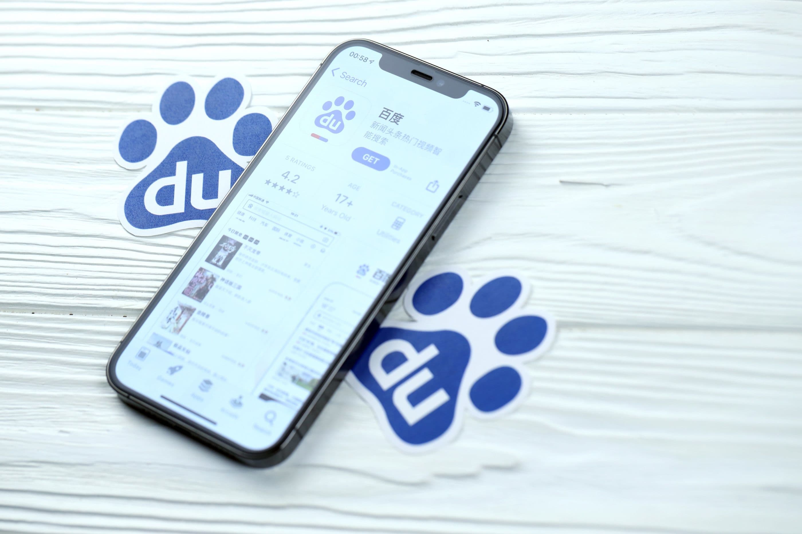 Baidu-Symbol und Anwendung aus dem App Store auf dem iPhone 12 pro Display auf einem weißen Holztisch