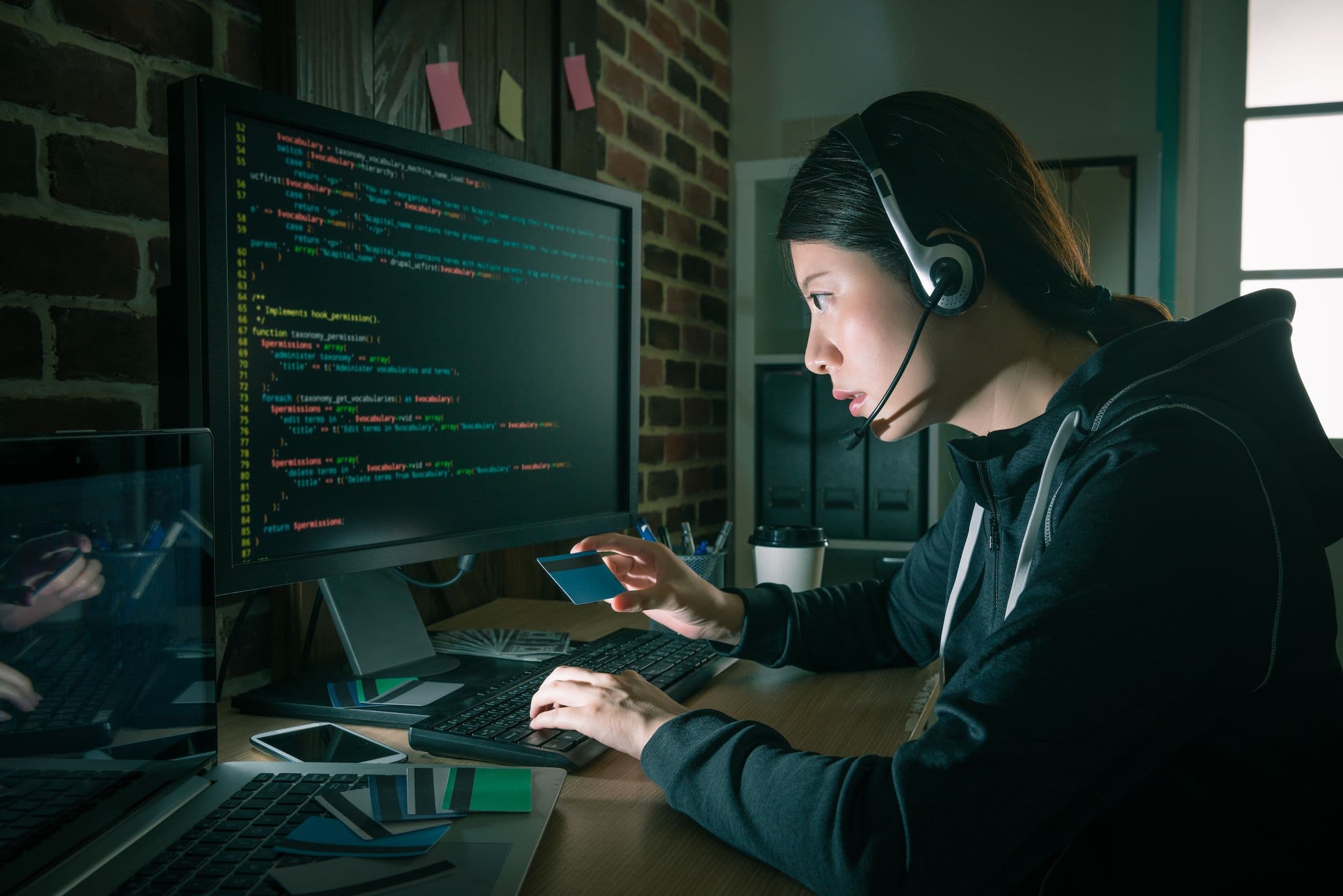 Chinesisches Hackerin mit Kopfhörer und Kreditkarte in der Hand beim Telekommunikationsbetrug