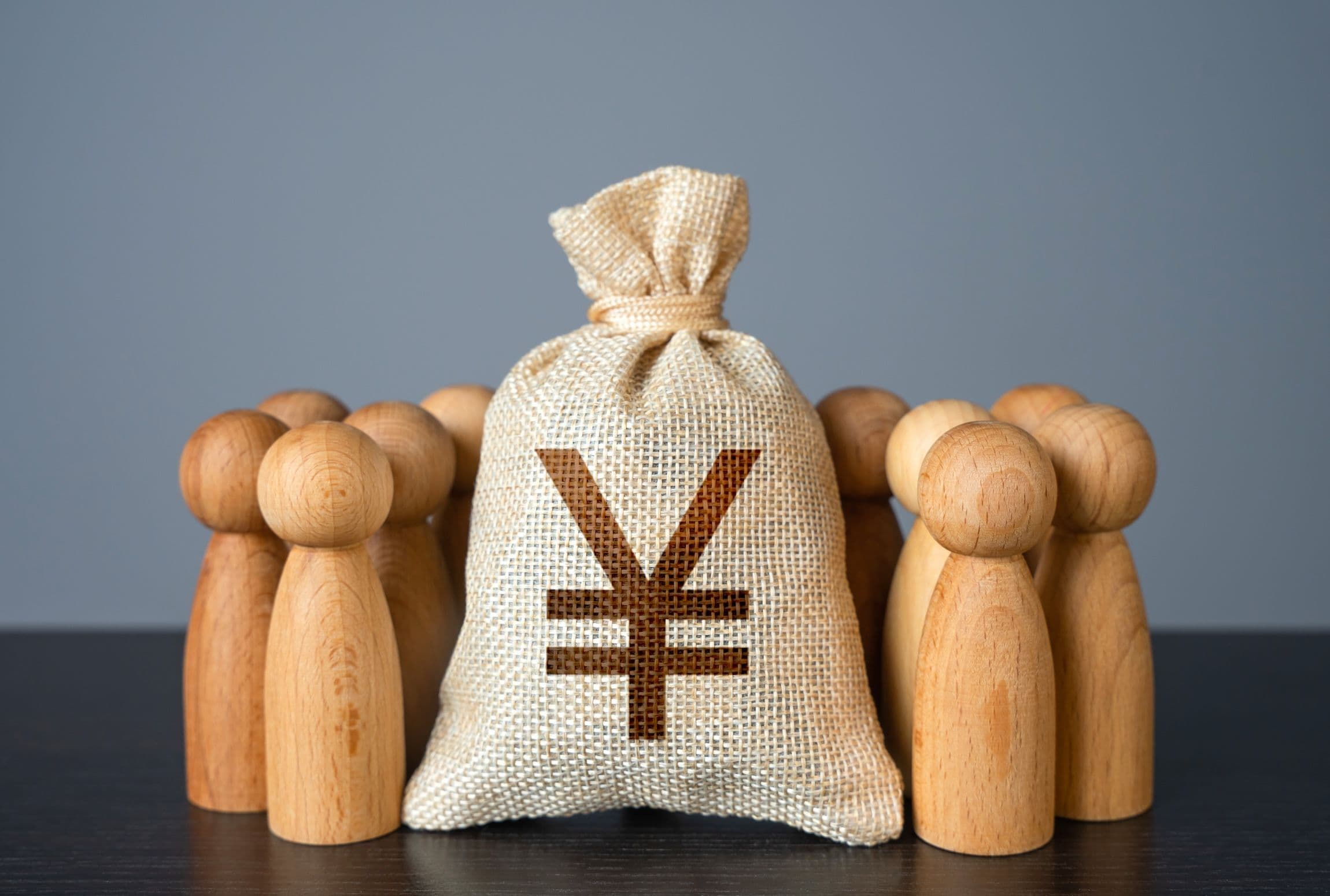 Holz Figuren in Form von Menschen stehen um einen Jutesack mit Yuan Zeichen darauf herum