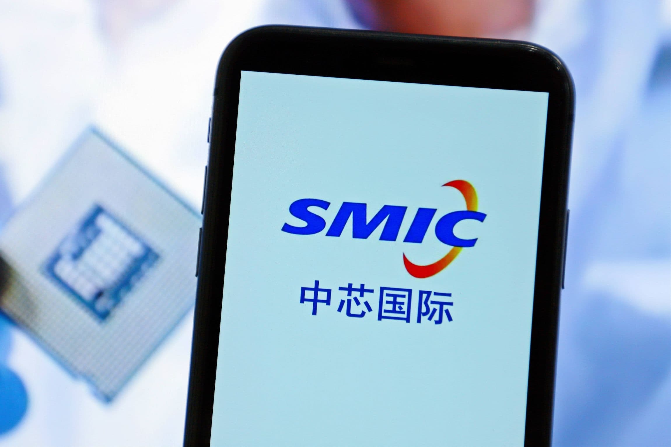 China Wirtschaft, Chipindustrie: SMIC Logo auf einem Smartphone, im Hintergrund sieht man einen Chip