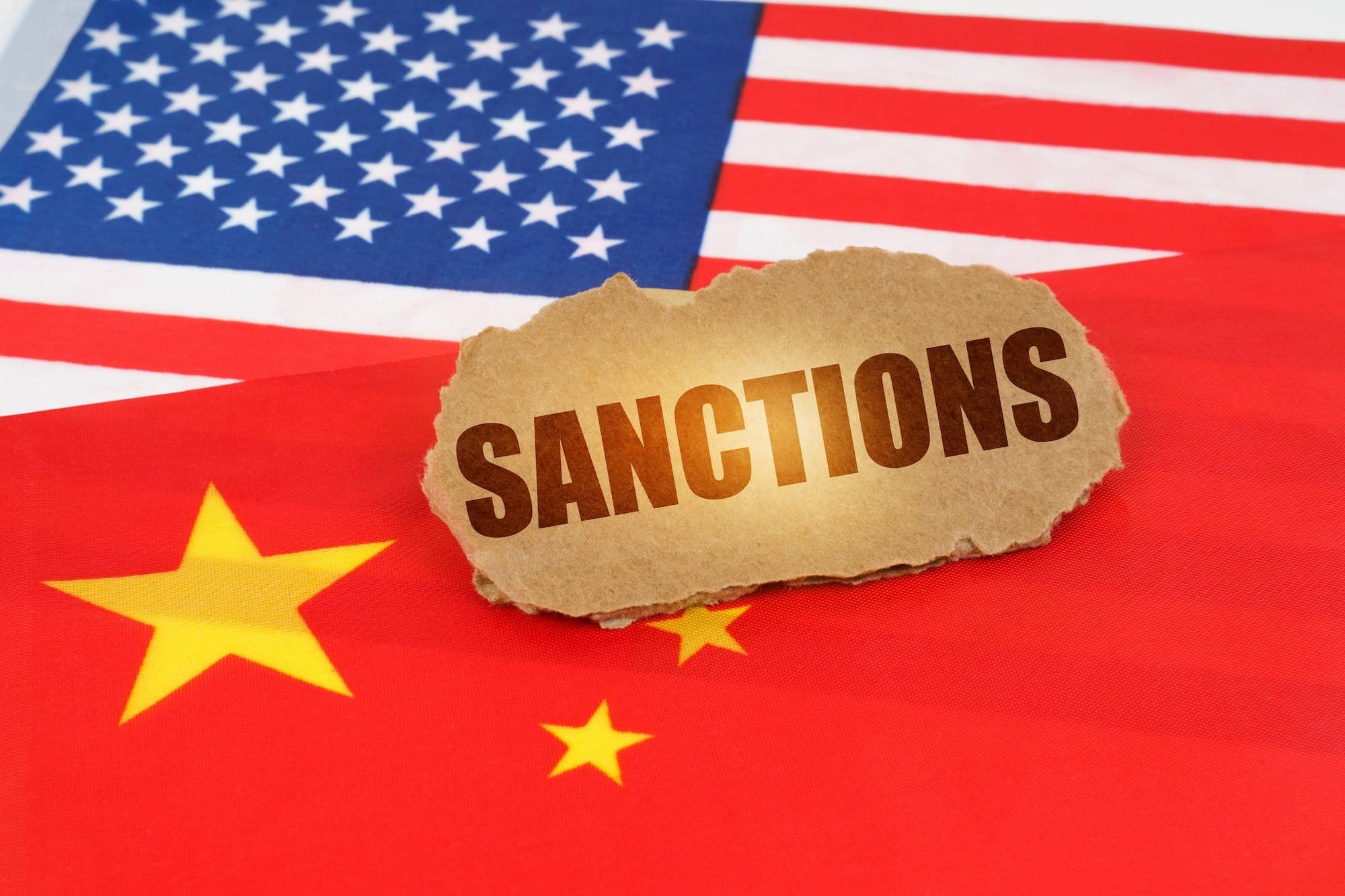 China USA Politik: Auf den Flaggen Chinas und der Vereinigten Staaten liegt ein Pappschild mit der Aufschrift - Sanctions