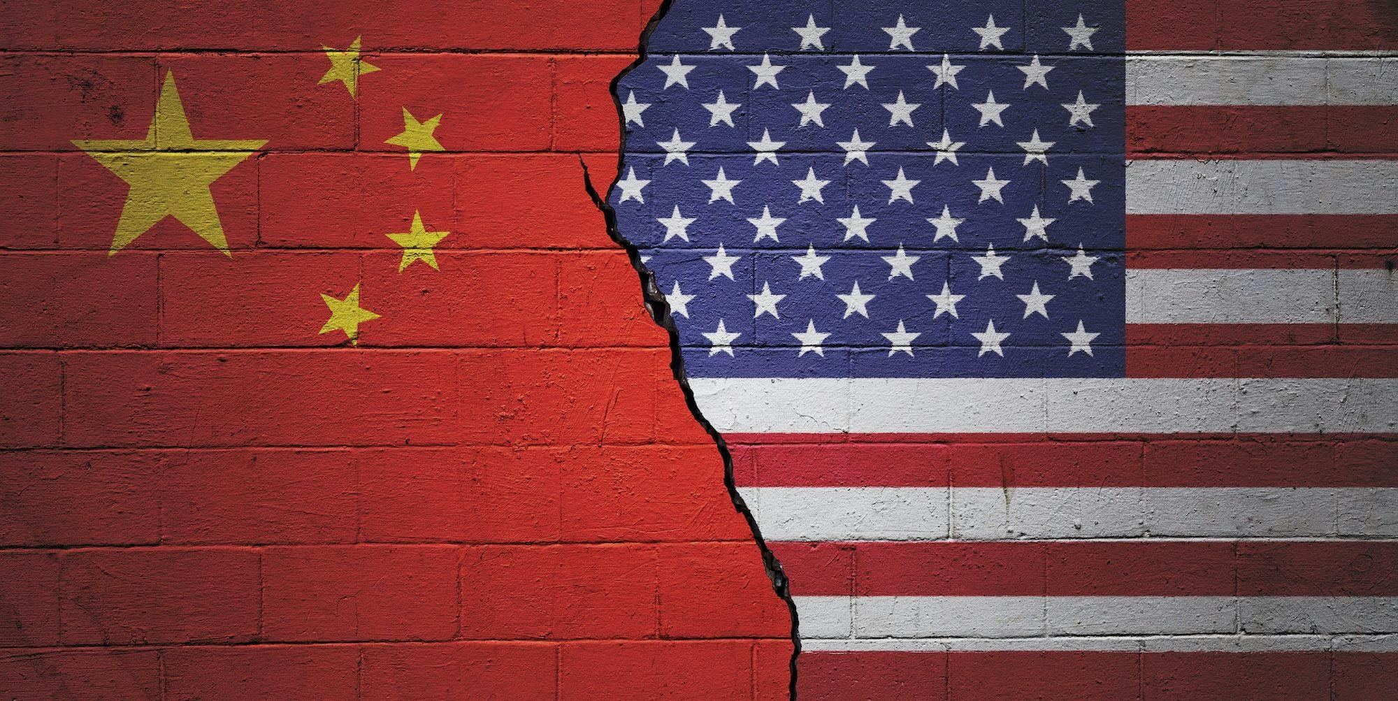 Politik China, China USA: Rissige Backsteinmauer, links mit einer chinesischen und rechts mit einer amerikanischen Flagge bemalt